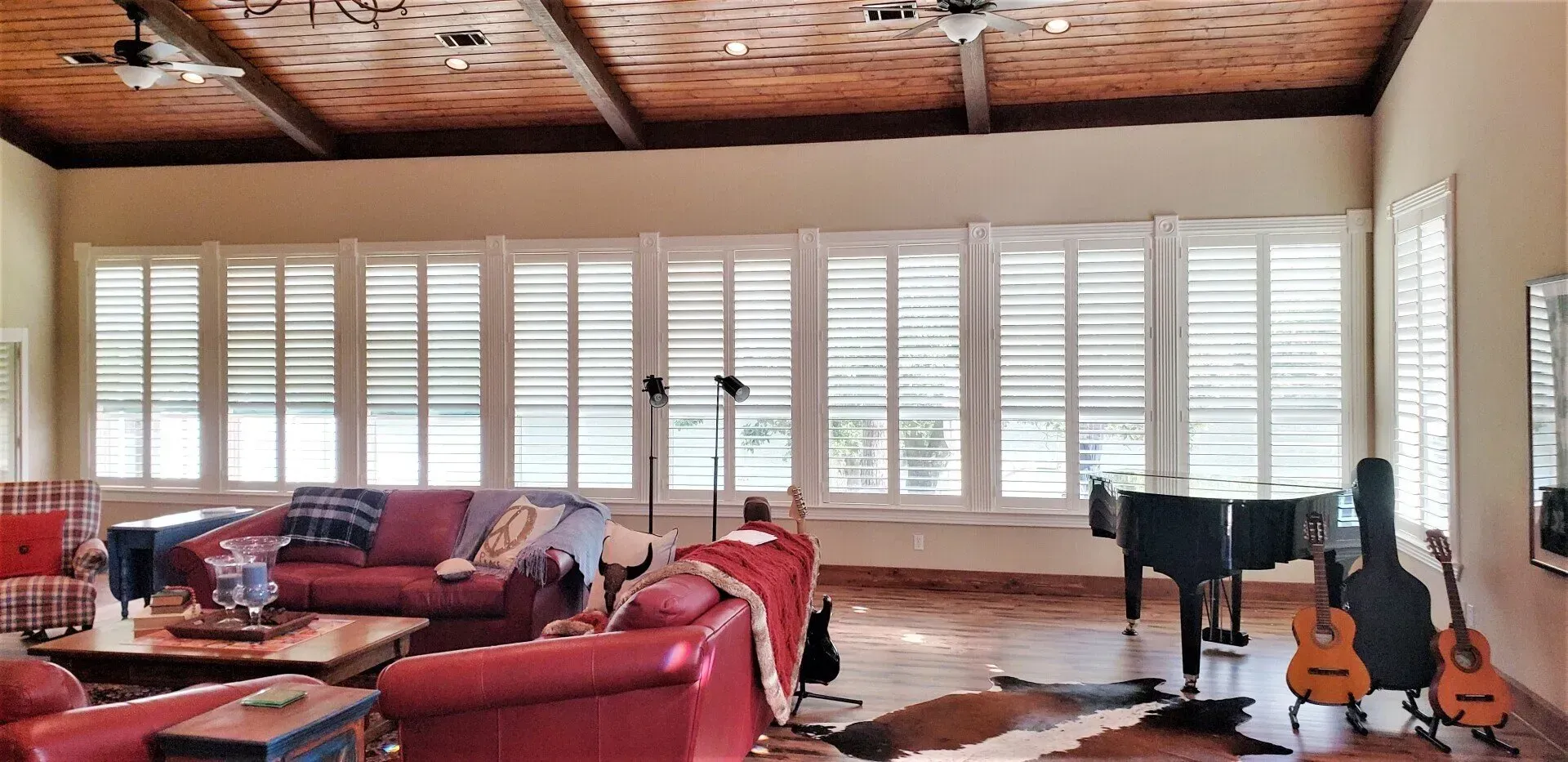 Bright living room with red sofas, white shutters, wood ceiling, and guitars by a window