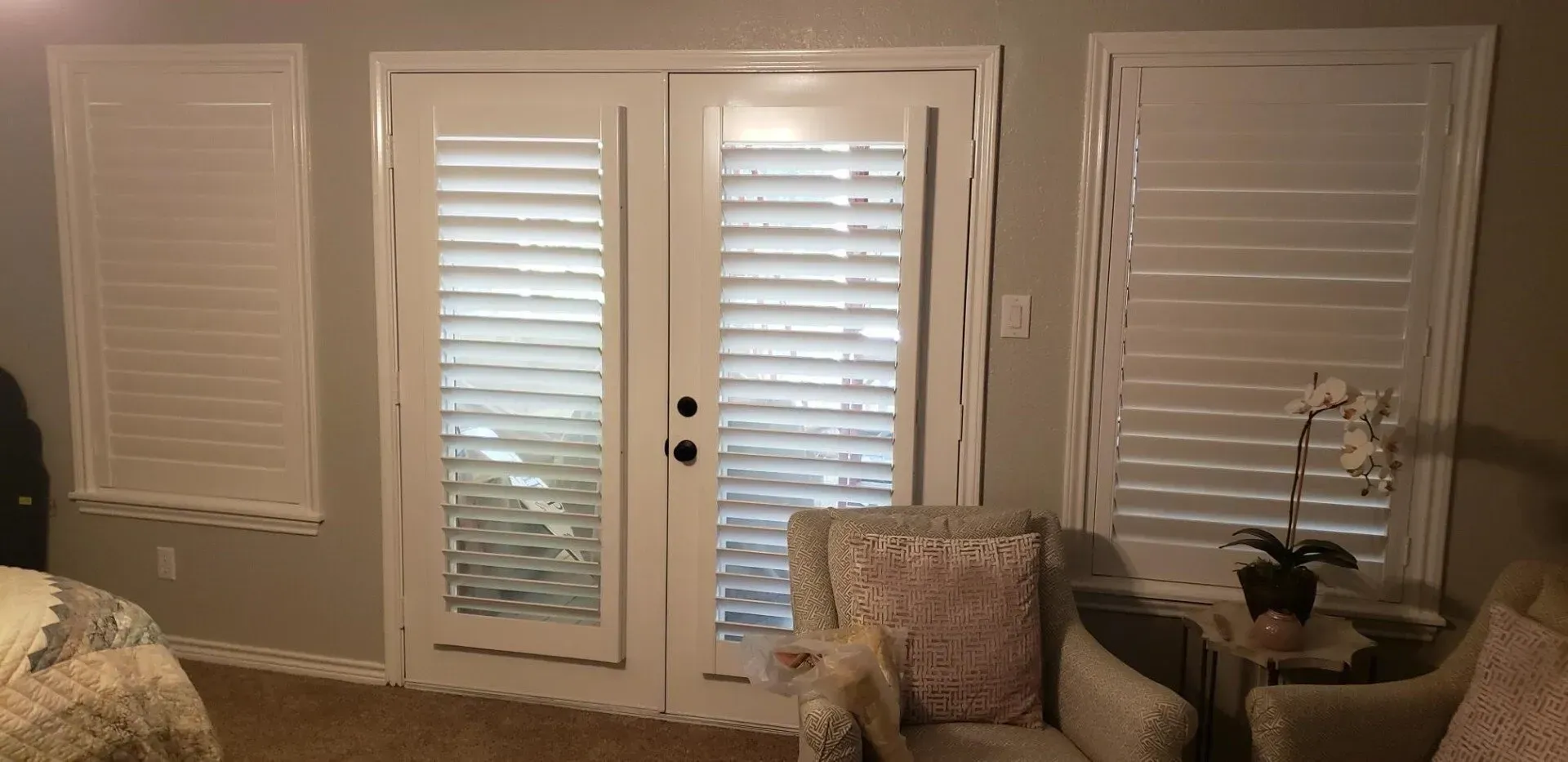 Cozy living room with French doors, white shutters, patterned chair, and potted plant by a couch