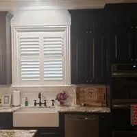 Modern kitchen with white farmhouse sink, dark cabinets, granite counters, and a window with shutters