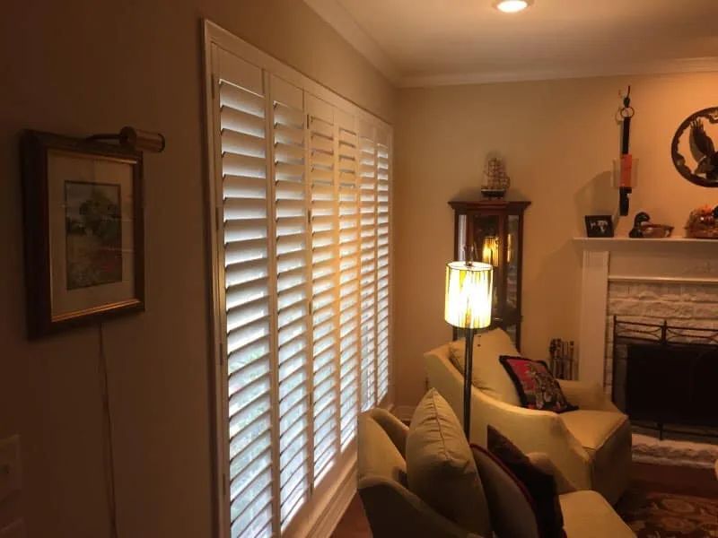 Cozy living room with beige sofa, lit lamp, shutters, fireplace, and framed wall art