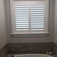 Bathroom window with white shutters above a tiled tub surround