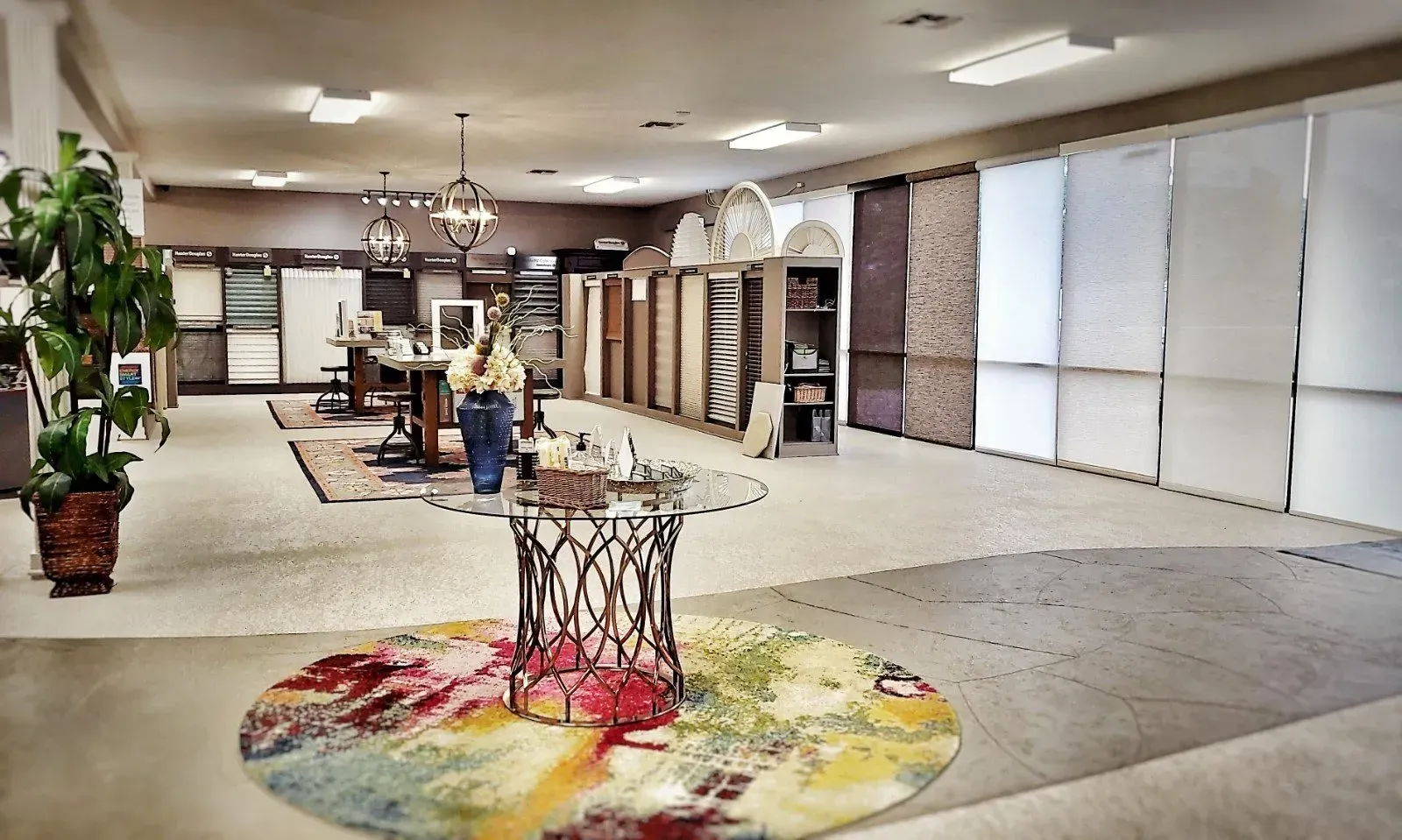 Interior of a carpet showroom with display racks, rugs, and potted plants on a beige floor