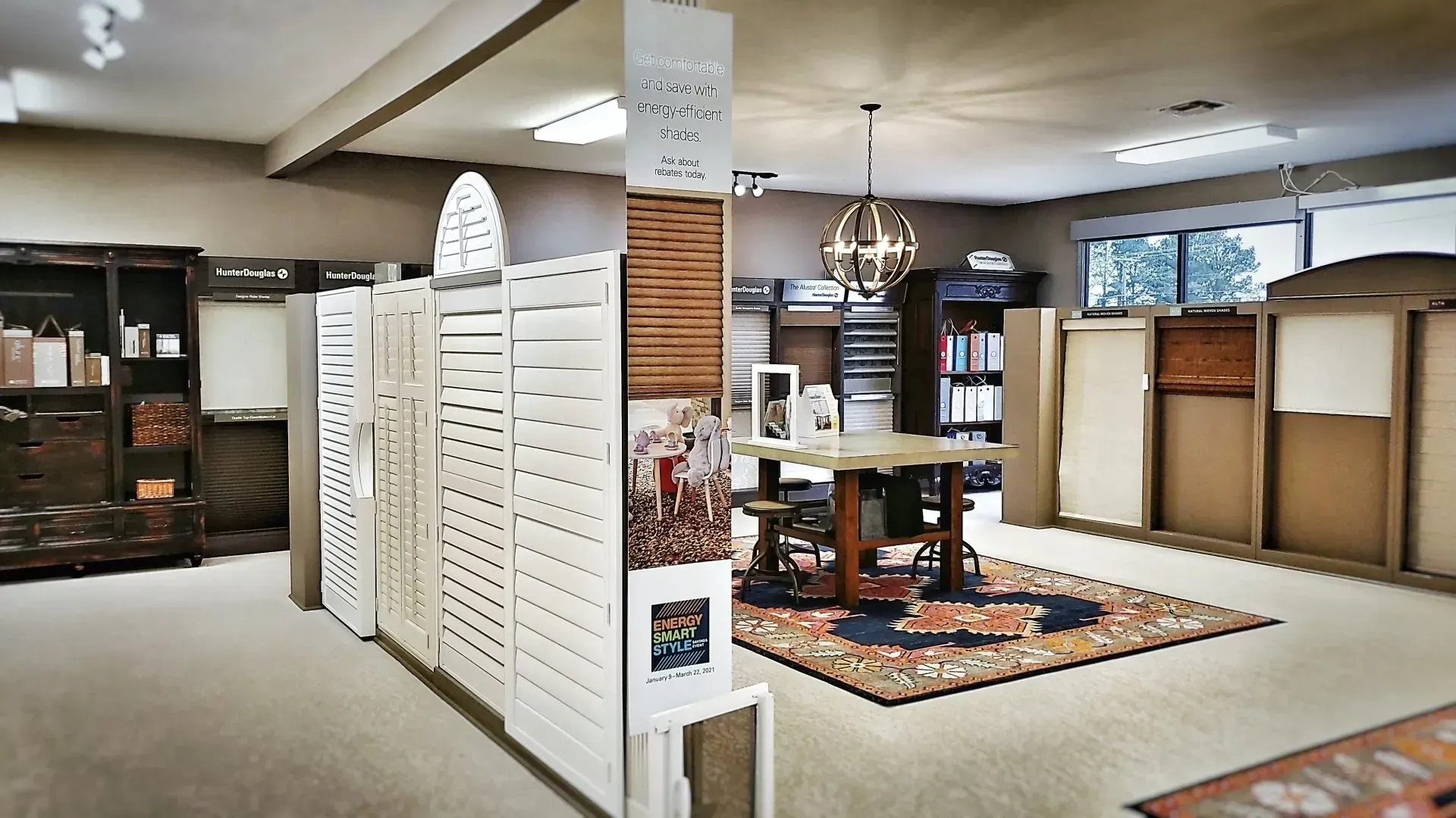 Spacious furniture showroom with display tables, cabinets, and rugs under bright ceiling lights.