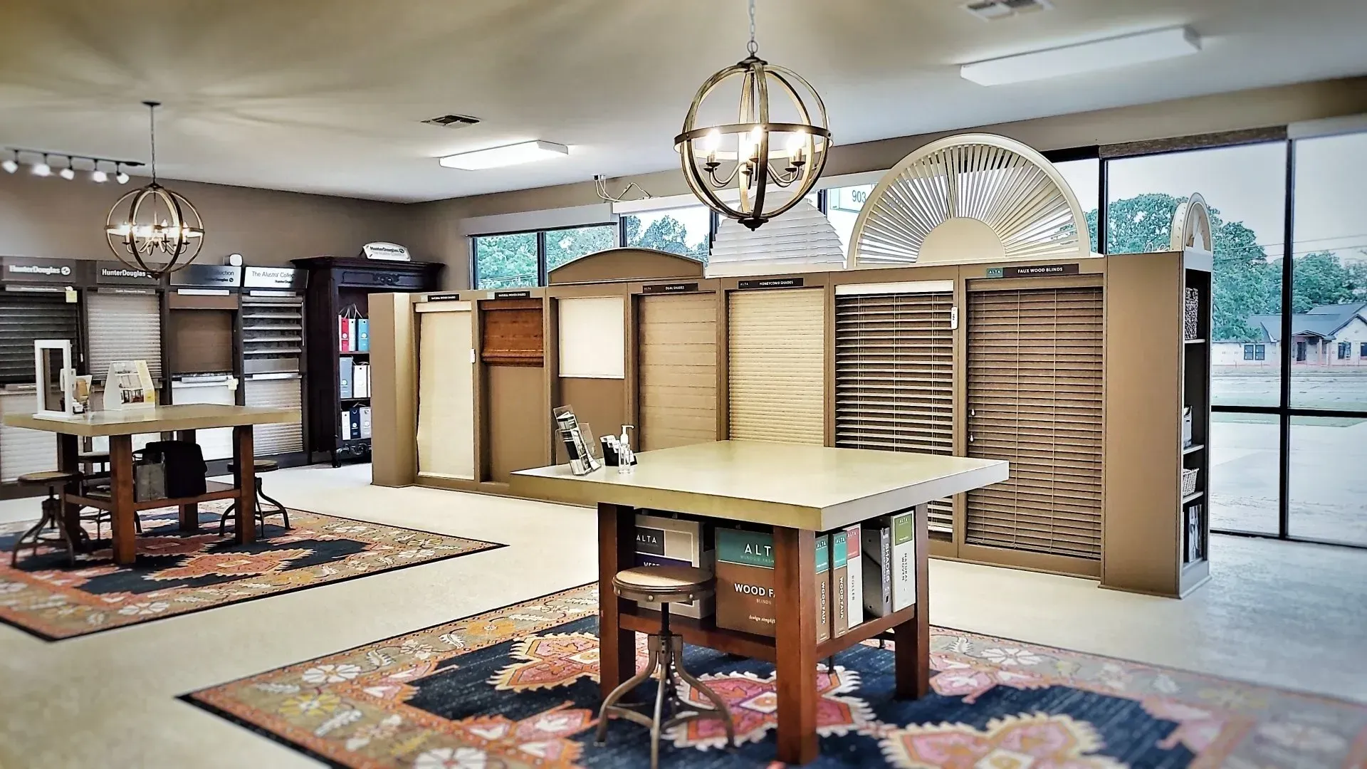 Furniture showroom with tables, display racks, and rugs in a bright room with large windows