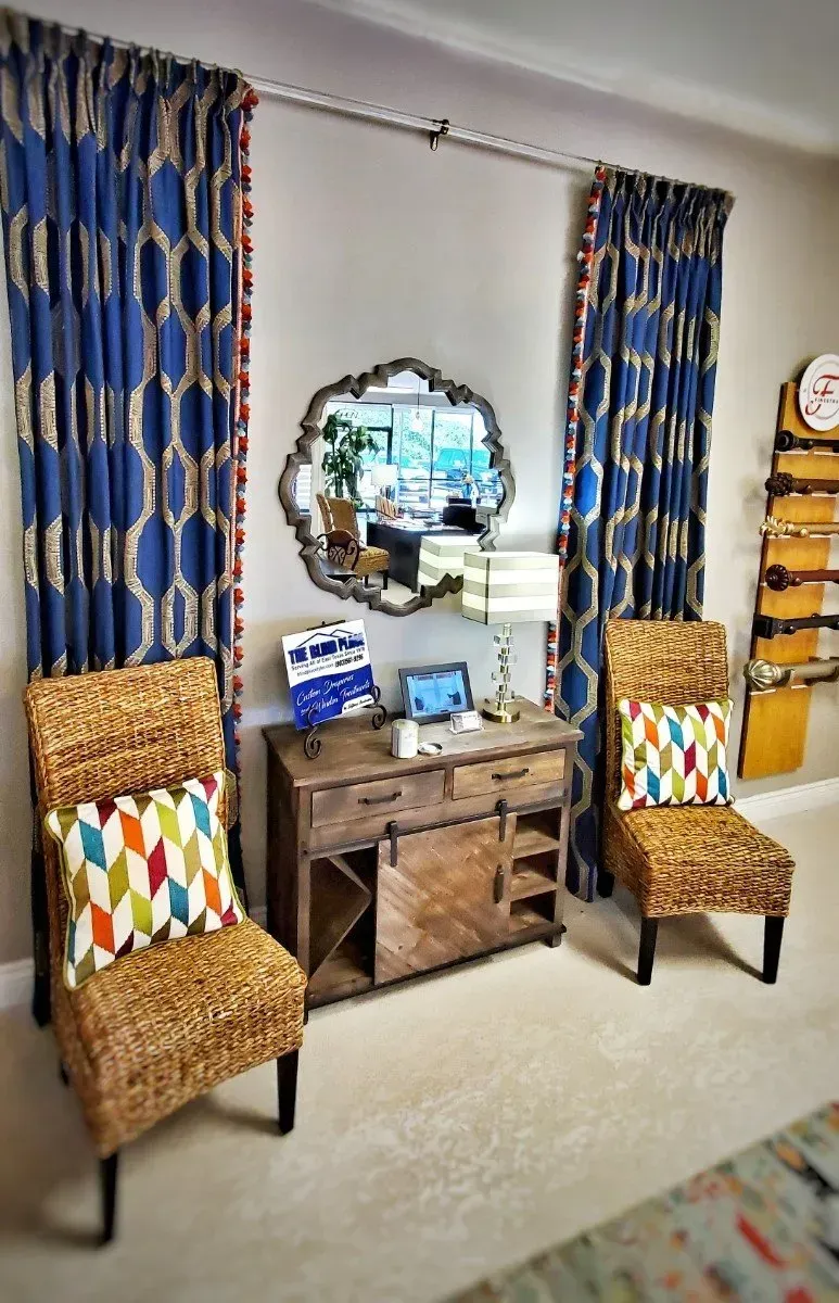 Cozy living room corner with wicker chairs, wooden chest, blue curtains, and ornate wall mirror