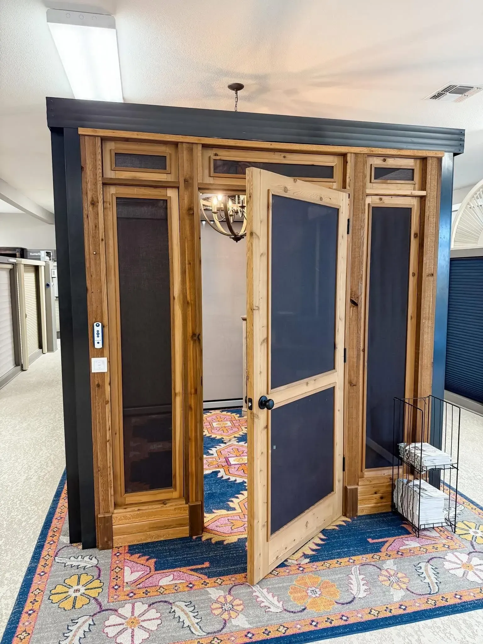 Wooden sauna booth with glass door, displayed indoors on a patterned rug.