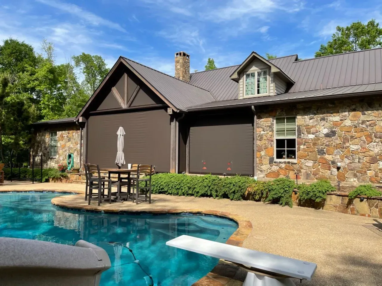 Backyard patio with a stone house, swimming pool, and patio table with umbrella.