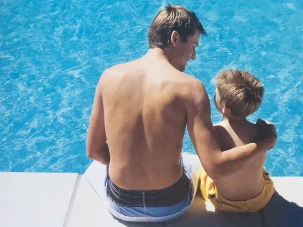 A man and a boy are sitting next to a swimming pool