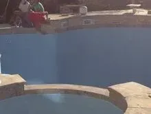 A person is sitting on the edge of a swimming pool.