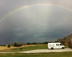 A white van is parked in a driveway under a rainbow.