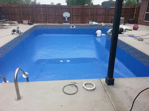 A large blue swimming pool with a wooden fence in the background