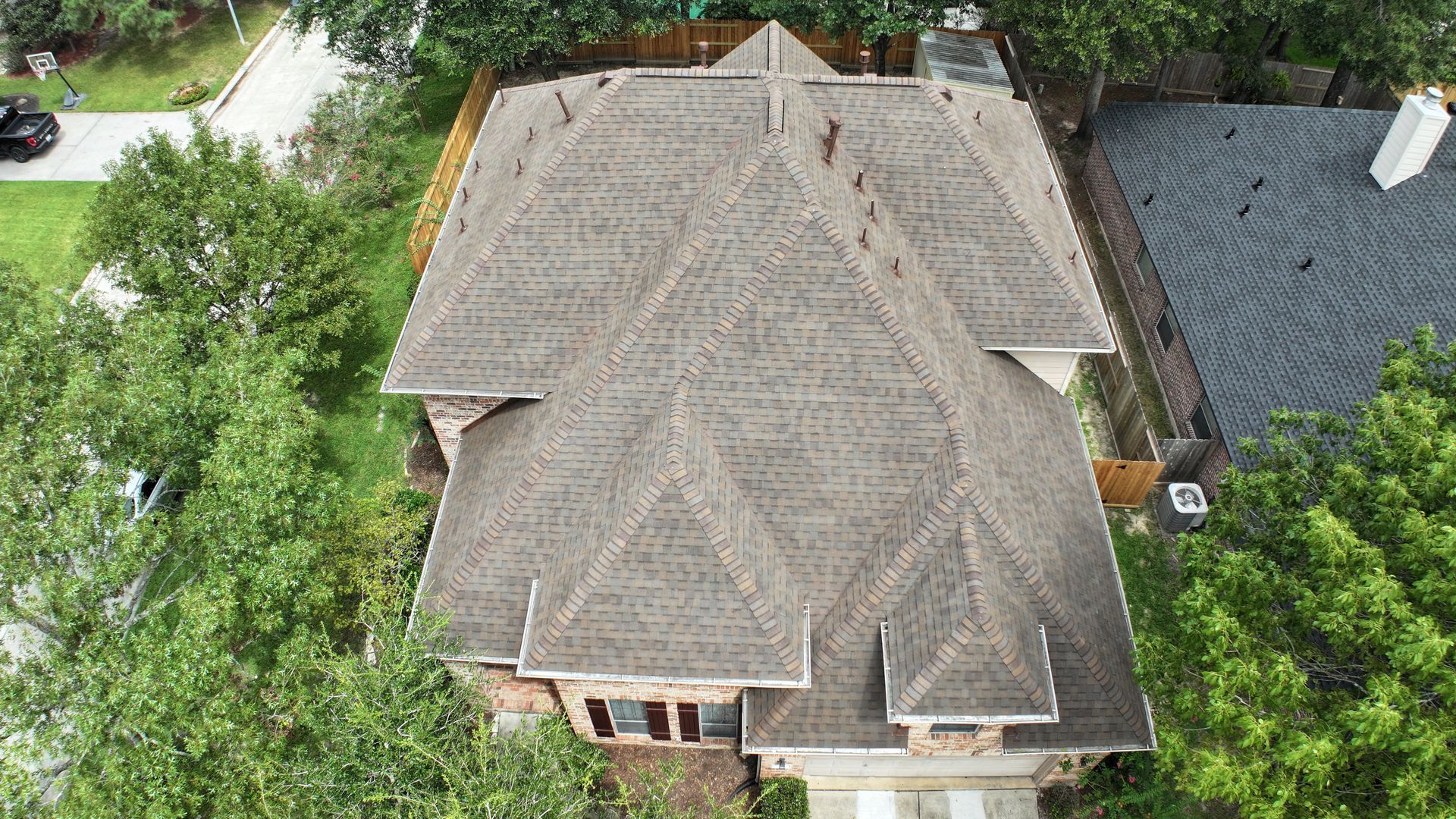 Aerial view of a multi-gabled brown roof on a two-story house surrounded by green trees.