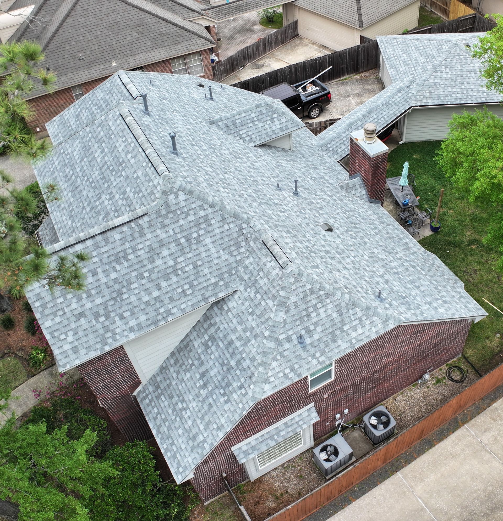 Aerial view of a house with a gray shingle roof, brick exterior, and a yard with trees