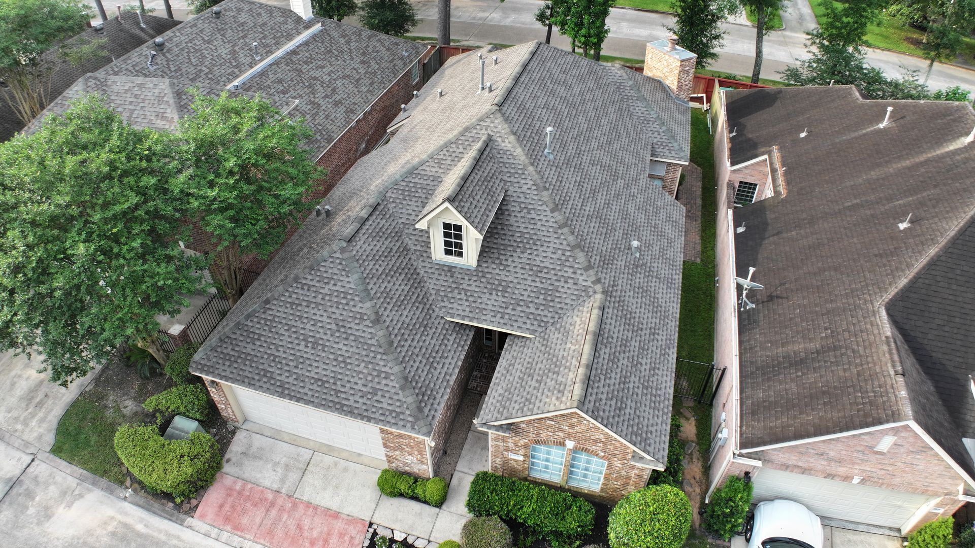 An aerial view of a two-story brick house with a gray roof and a small dormer.