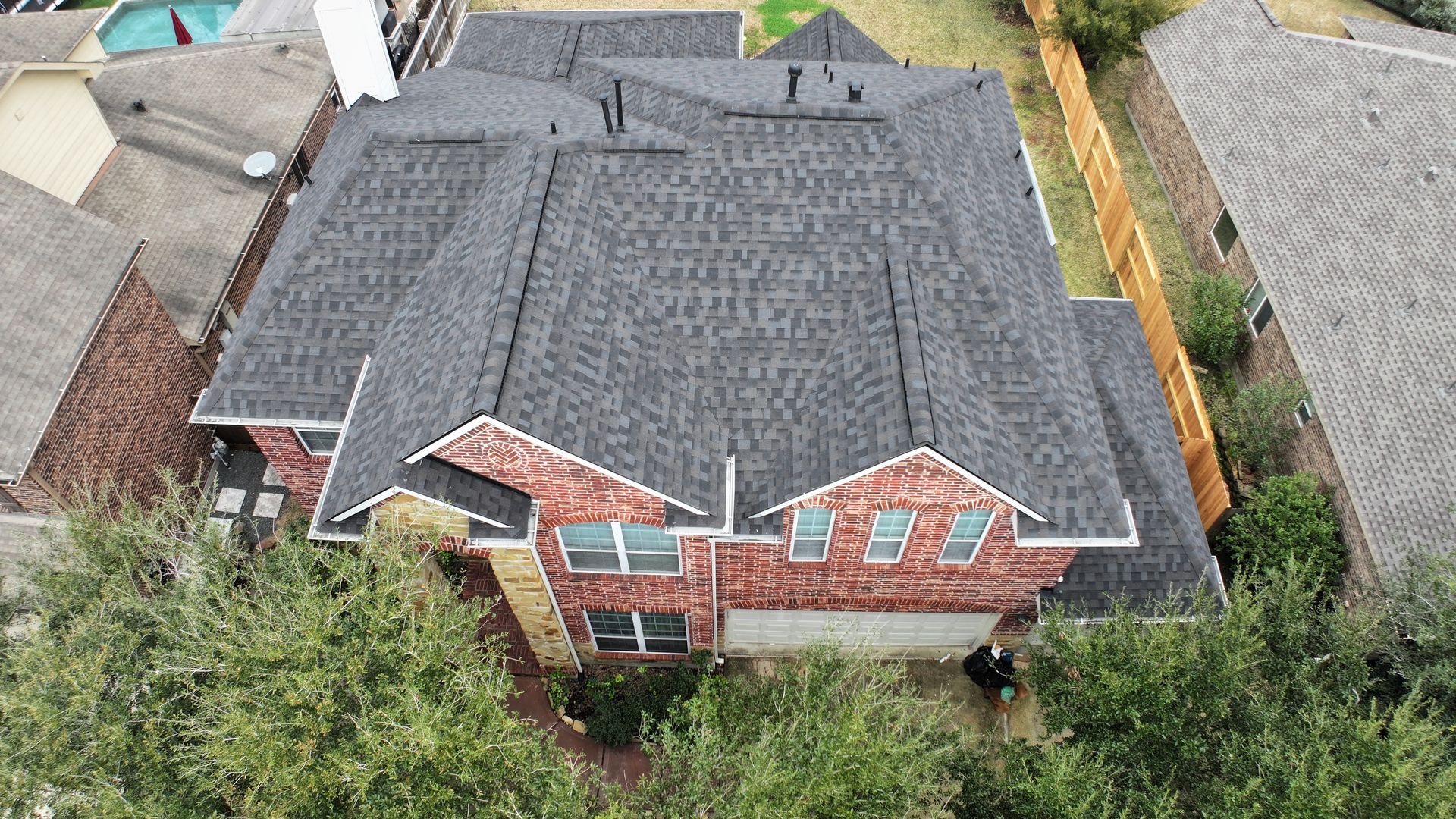 Overhead view of a two-story brick house with a dark gray roof and a fenced backyard.