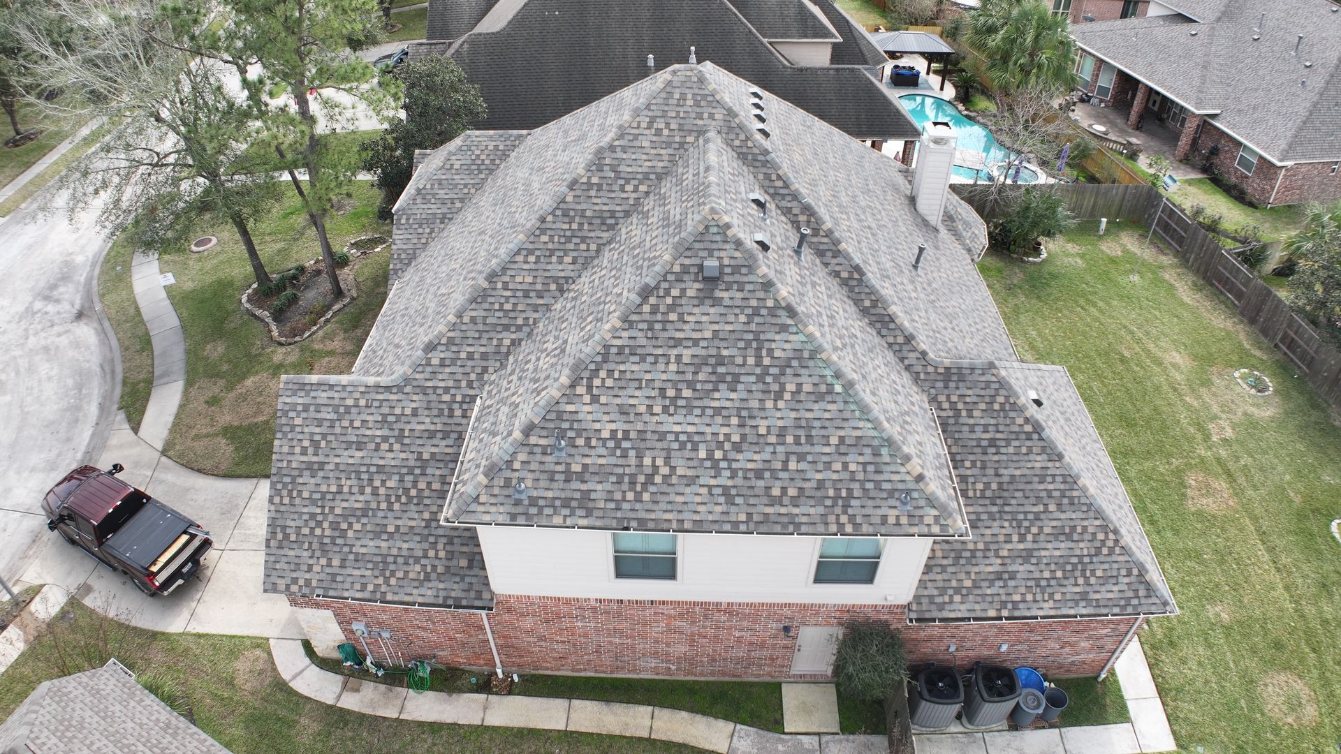 Aerial view of a brick house with a gray roof, a pool, and a truck parked in the driveway.