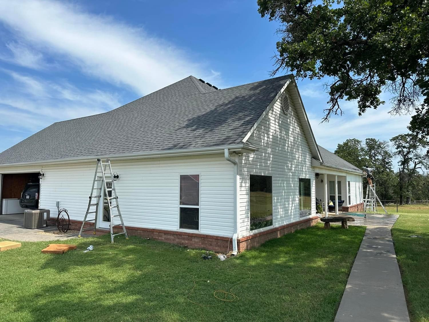 White house with dark gray roof, ladder, and green grass on a sunny day.