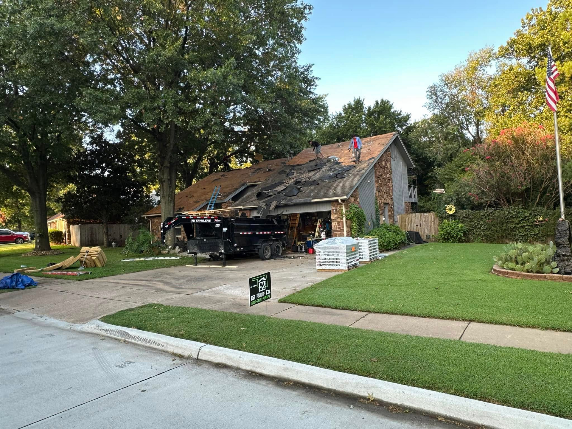 House with partially removed roof, construction debris, dump trailer, and an American flag.