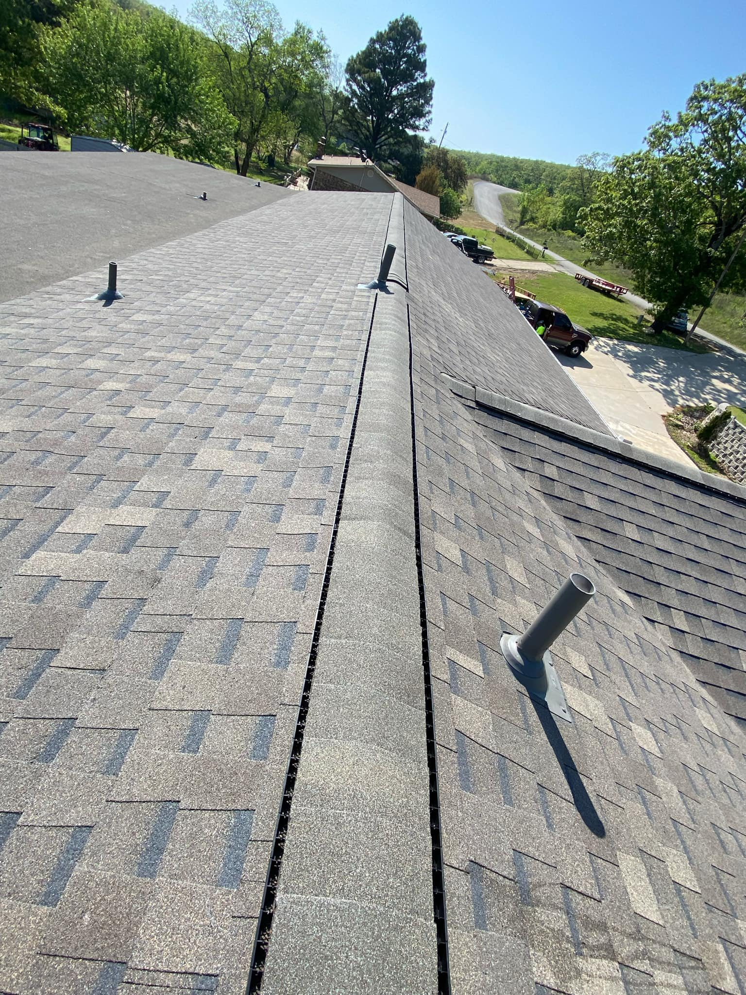 A rooftop with gray shingles and vents, a valley in the center, and a driveway in the background.
