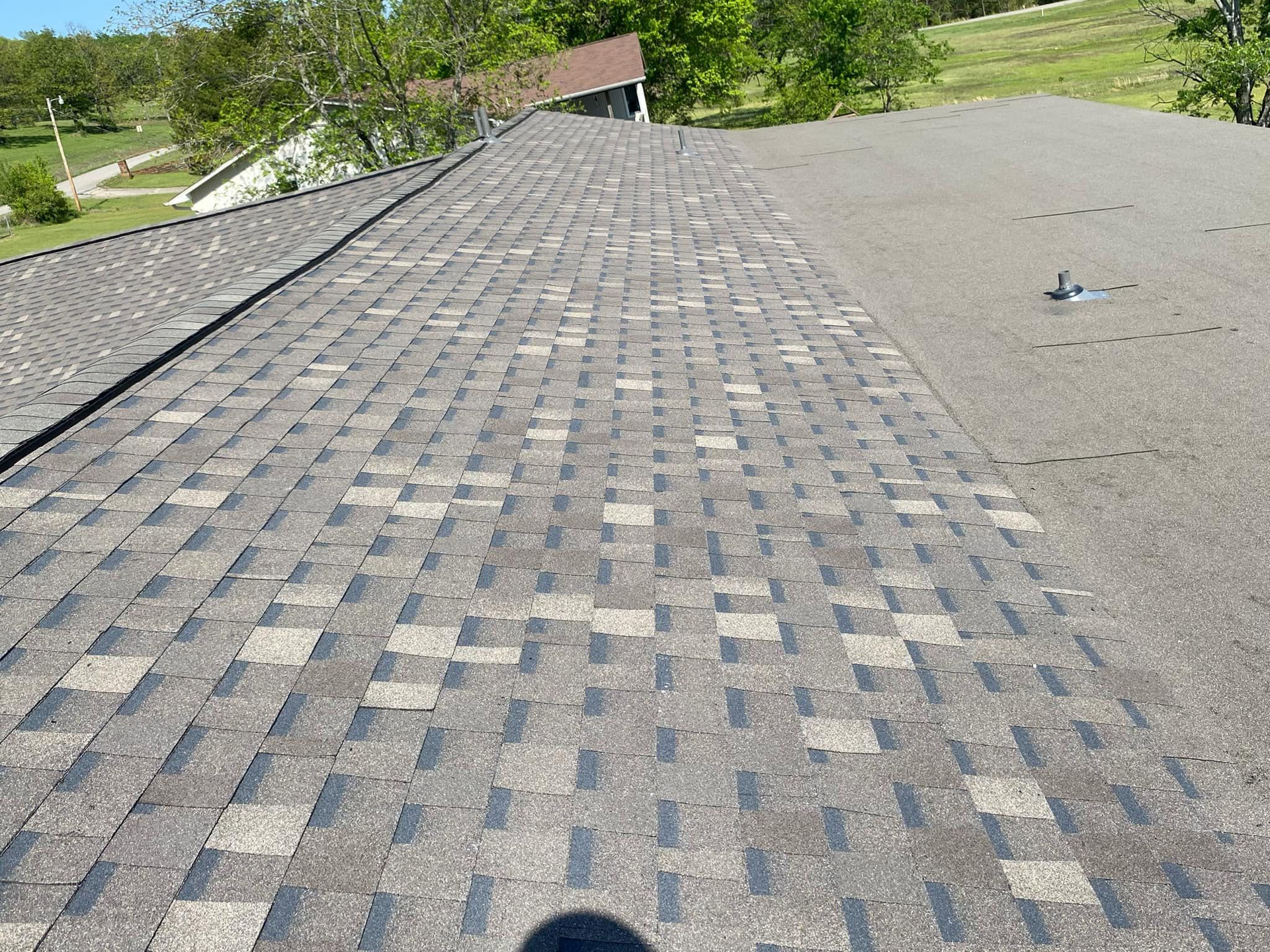 Overhead view of a roof with faded asphalt shingles. Some shingles are missing, and others are discolored.