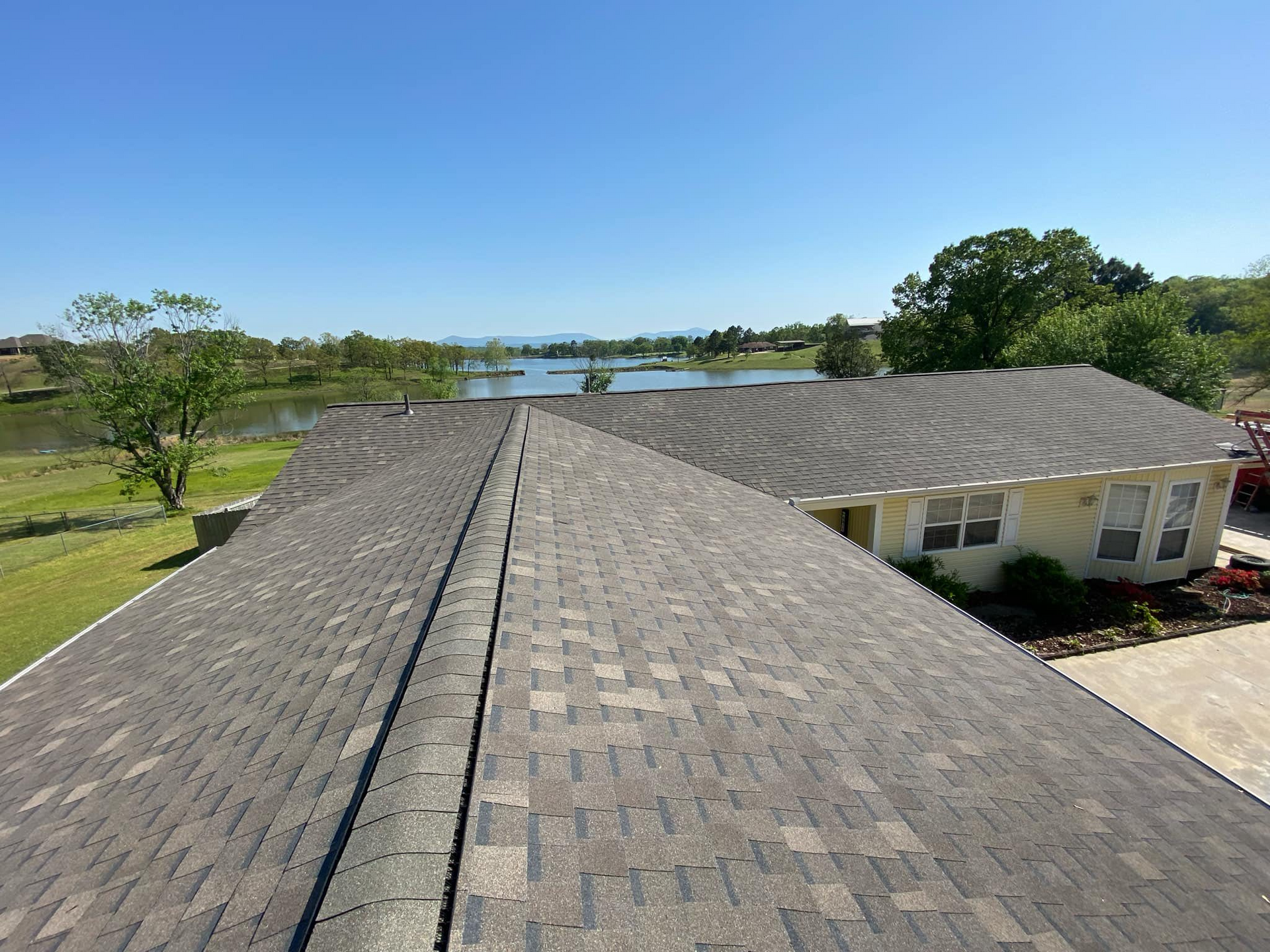 Overhead view of a house roof with a lake in the background under a blue sky.