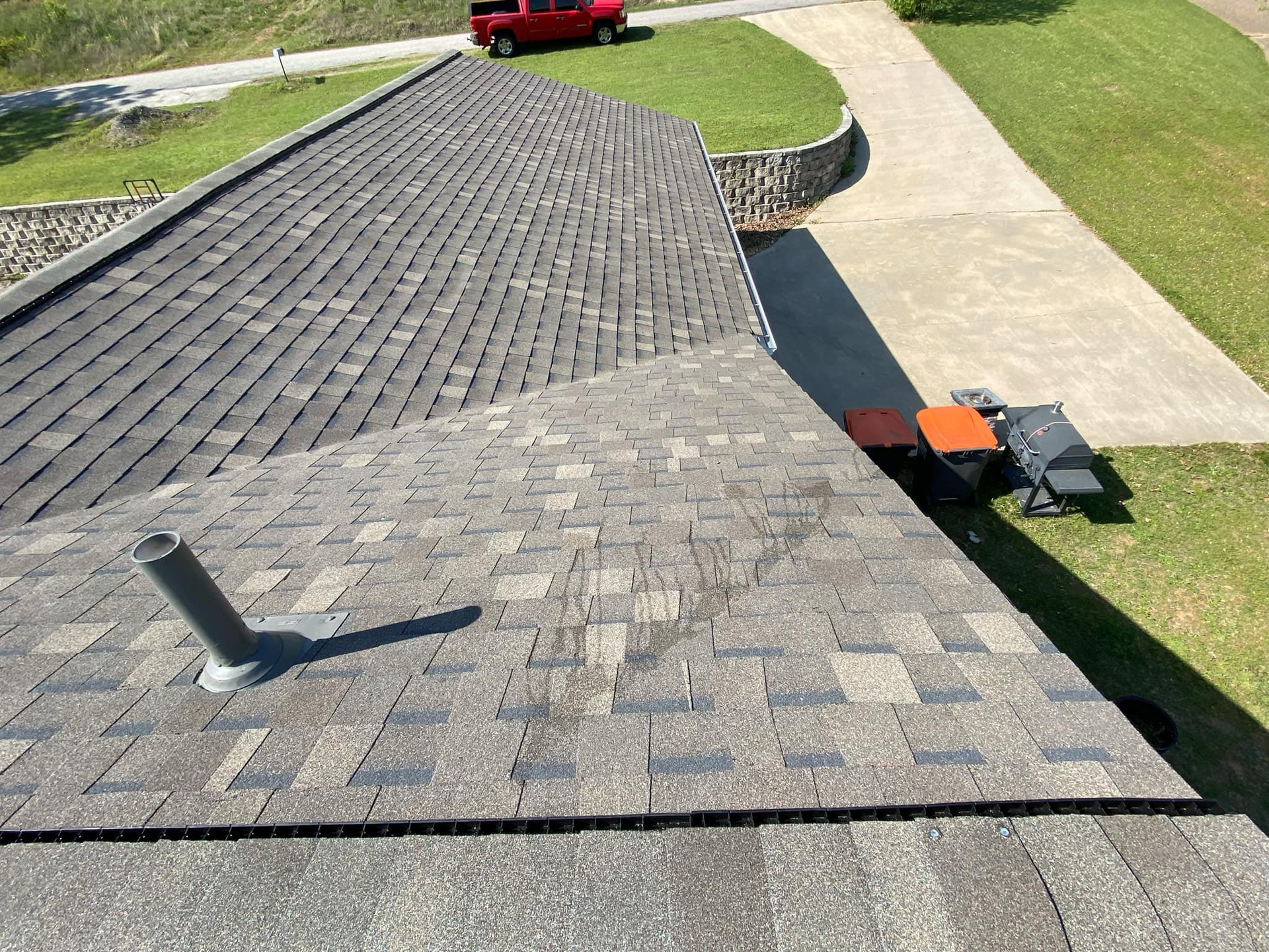 View of a shingled roof with a vent pipe, next to a driveway and grassy yard.