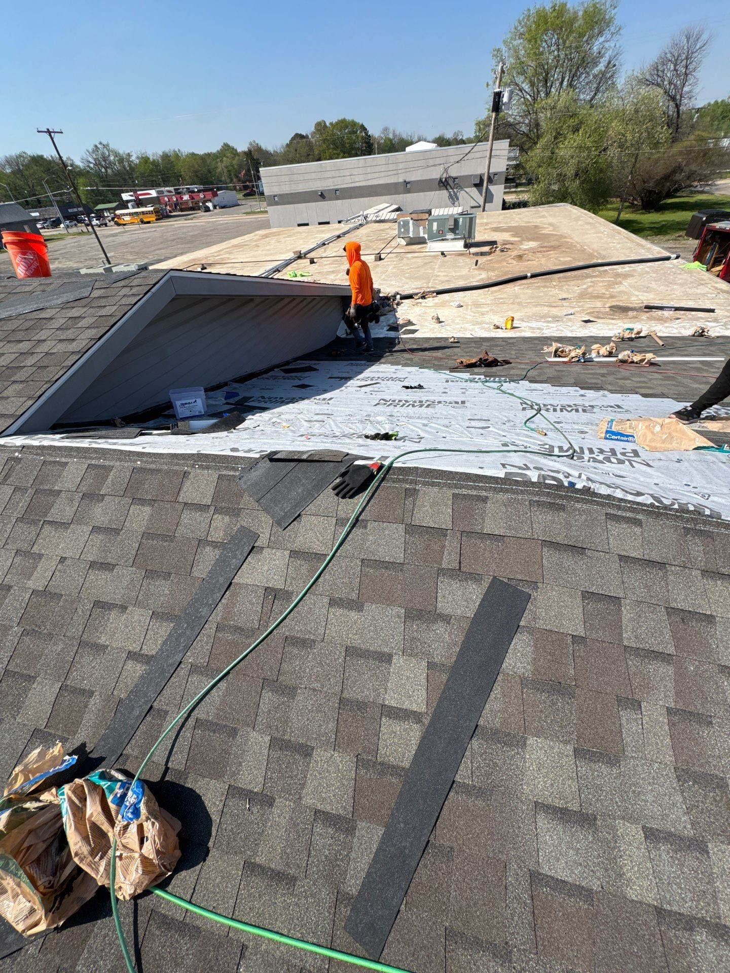 Roofers working on a residential roof, some asphalt shingles, blue sky, safety gear.
