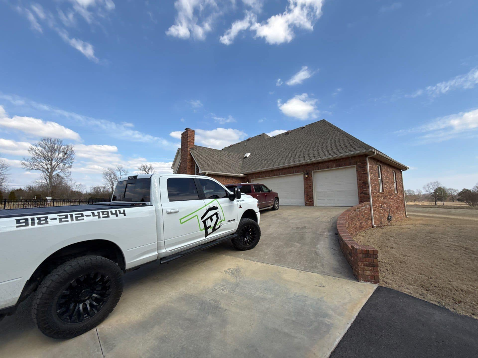 White pickup truck with company logo parked in front of a brick house with a three-car garage on a sunny day.