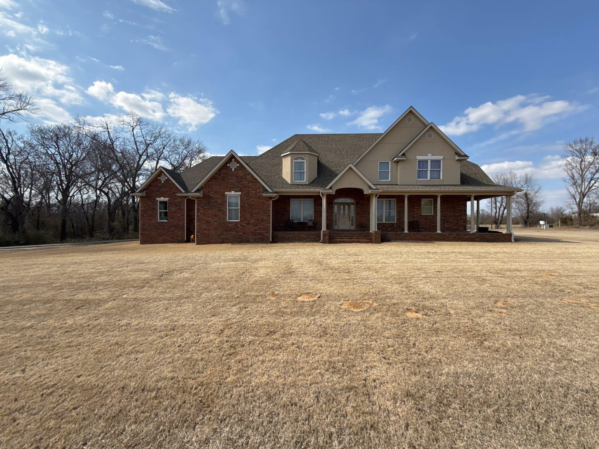 Two-story brick and beige house with porch, set in a field under a blue sky.