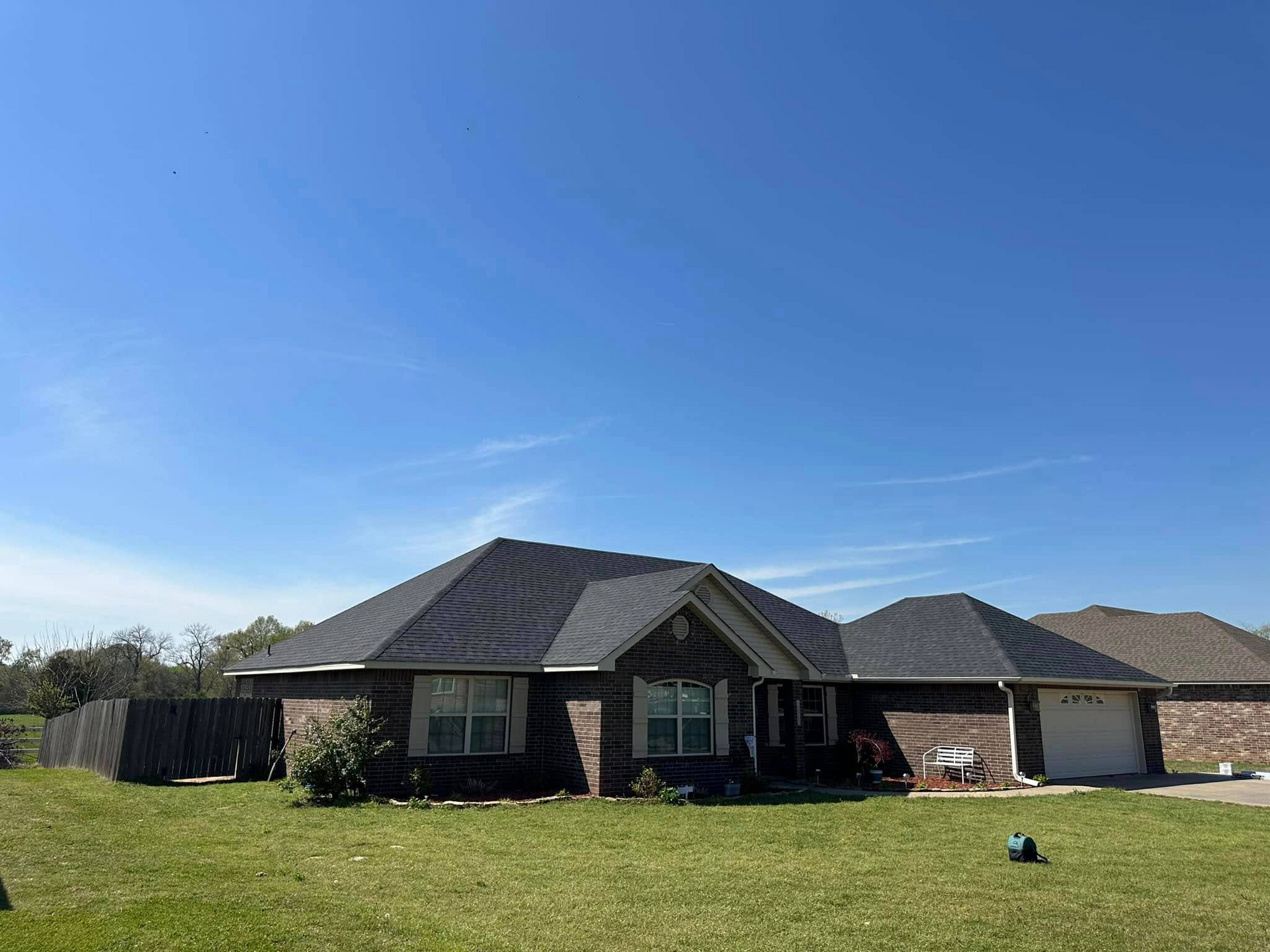 A one-story brick house with a dark roof on a sunny day with blue sky.