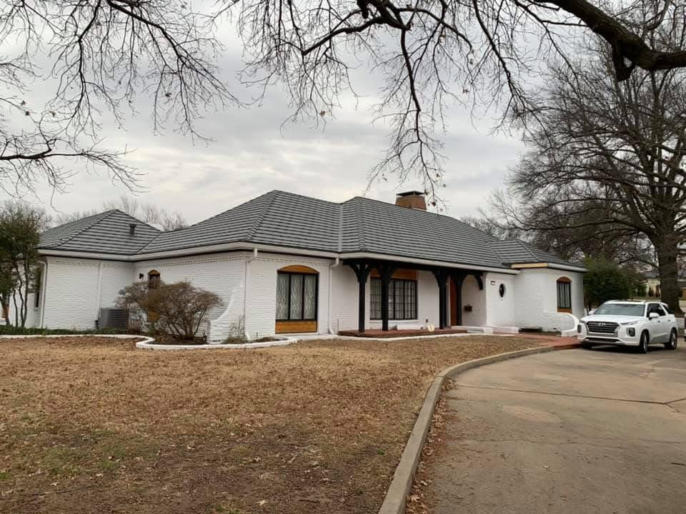White stucco house with dark roof, porch, and a car parked in the driveway. Overcast sky.