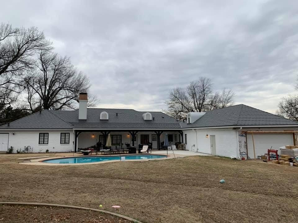 White house with a pool and dark roof. Cloudy sky. Backyard scene.