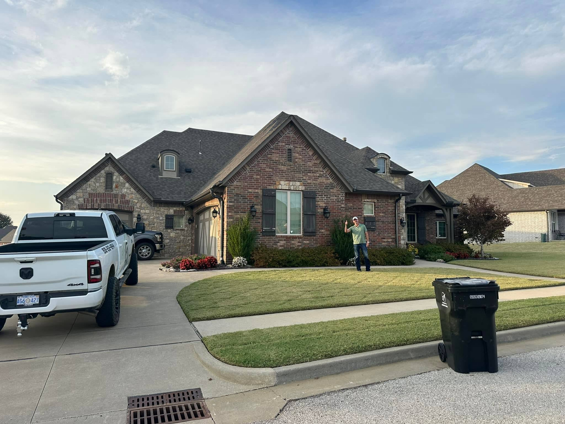 A brick house with a white truck parked in the driveway; a person waves from the lawn.