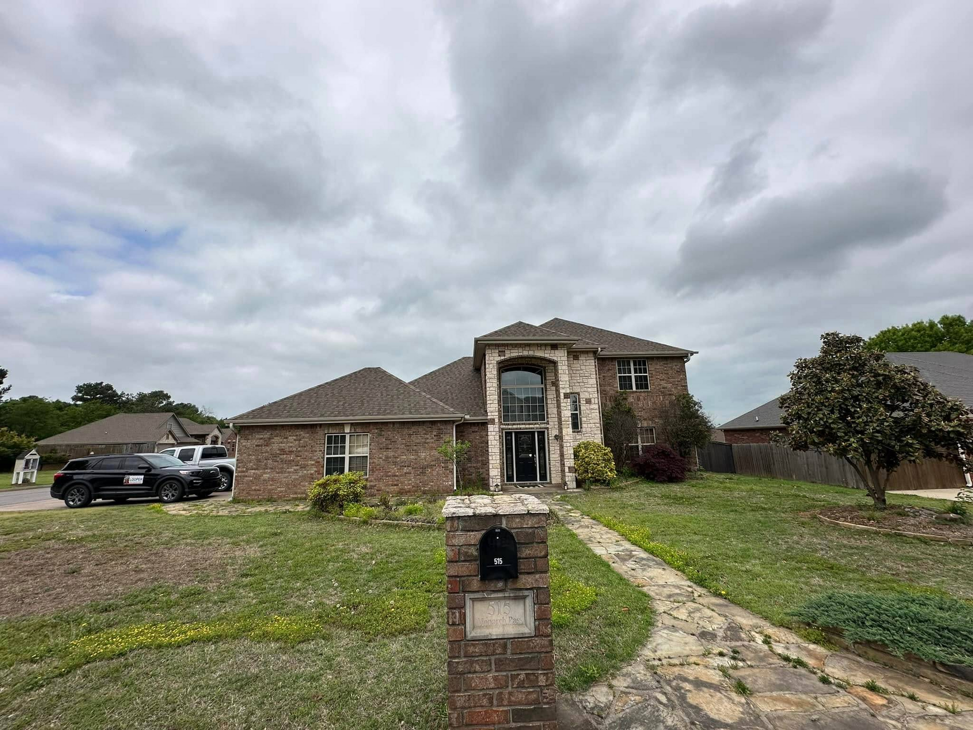 A brick house with a stone facade, cloudy sky overhead. A mailbox and a car in front.