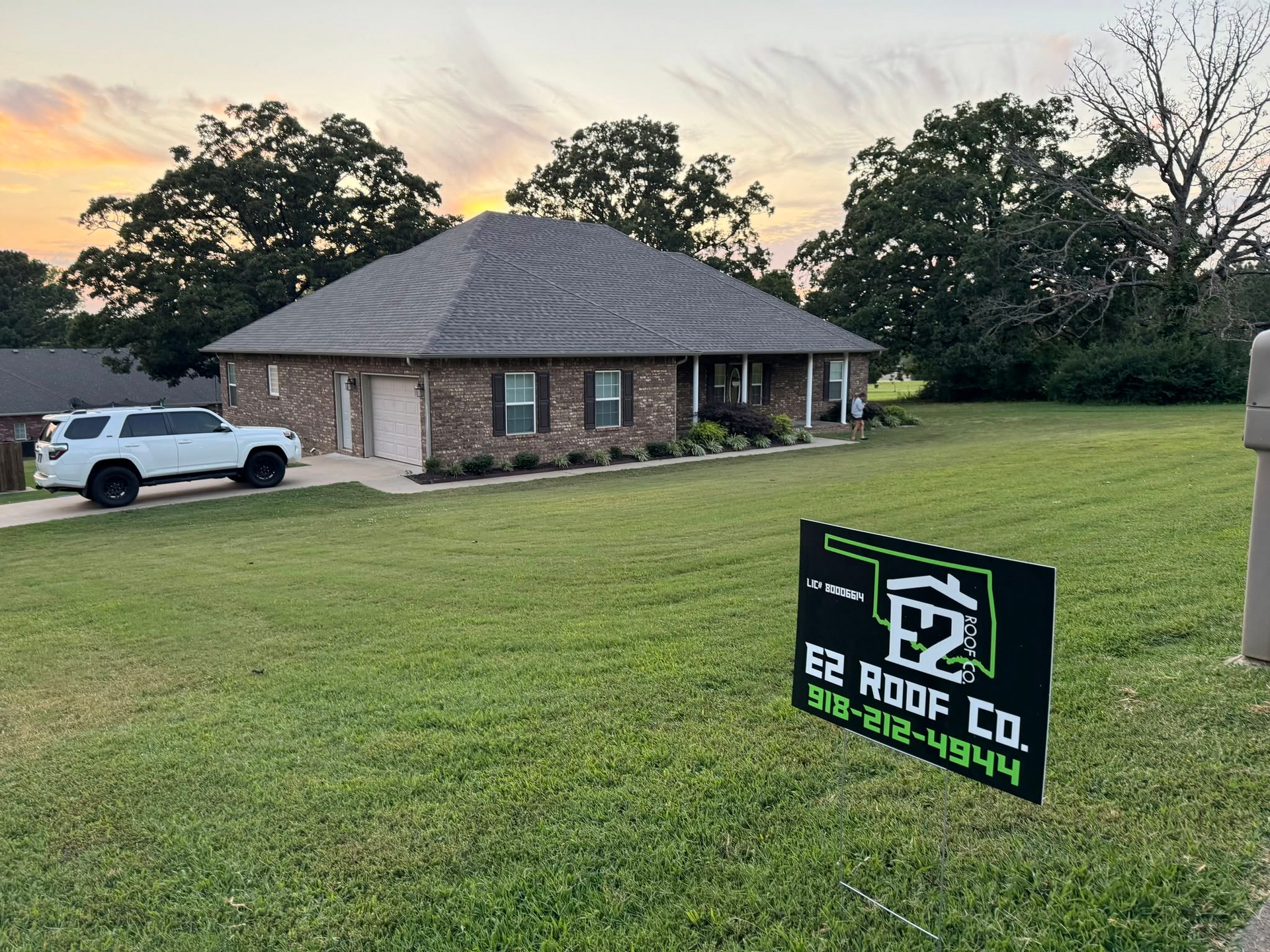 House with new roof and sign for E2 Roof Co. on lawn. White SUV parked in driveway.