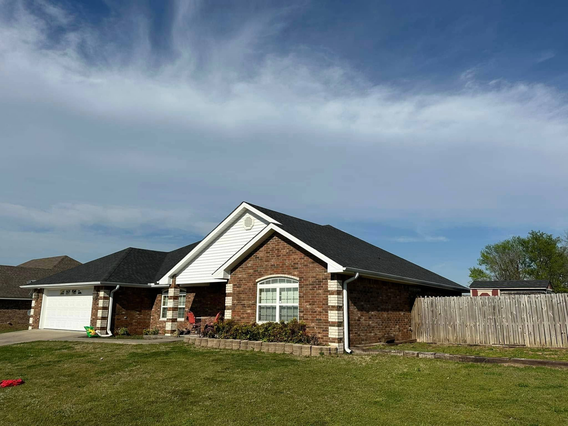 Brick house with dark roof and white trim under a cloudy sky.