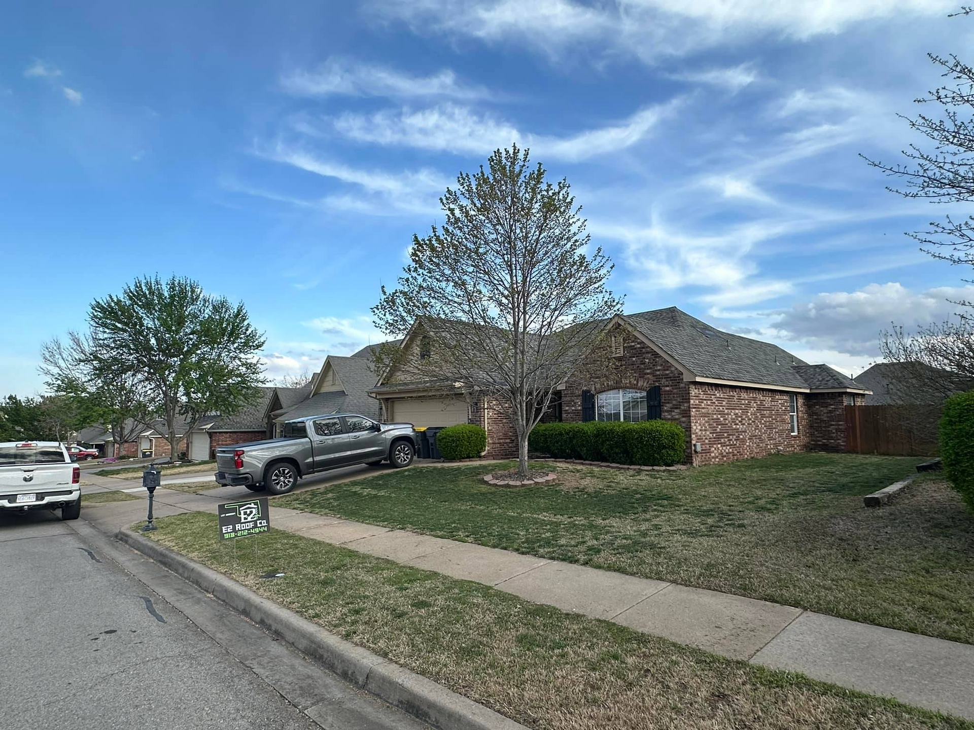 Suburban house with brick facade and green lawn on a sunny day with parked trucks.