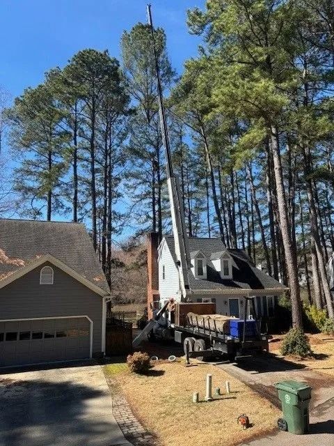 Tree removal crew operating a crane near a house beside tall pine trees