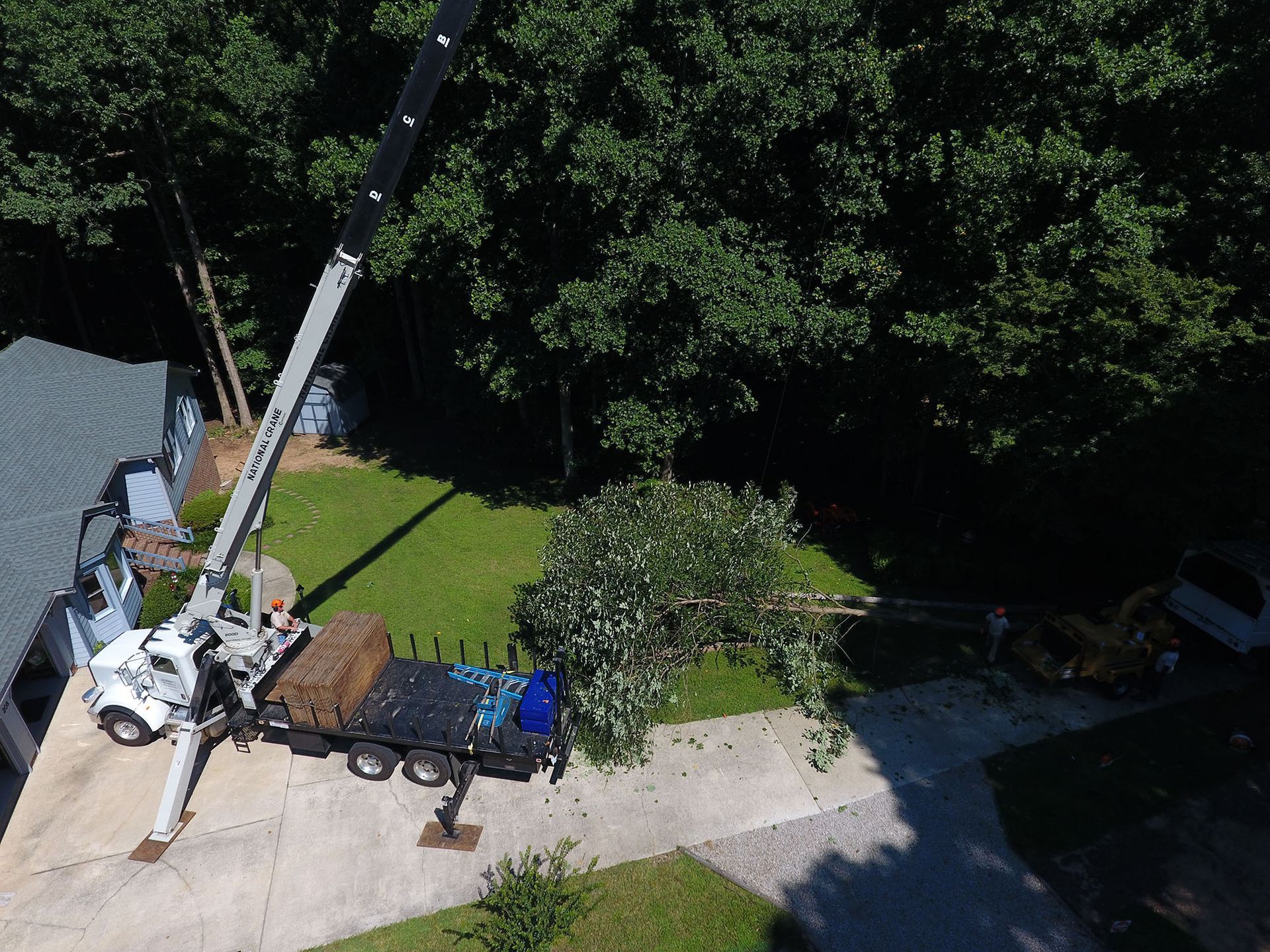 Crane truck lifting a tree stump near a driveway beside a house and lawn