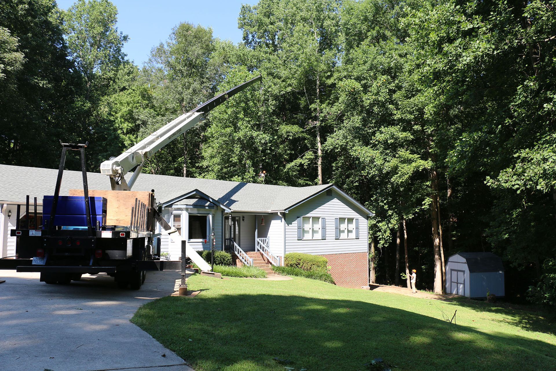Truck with extended crane parked in a driveway beside a house and trees
