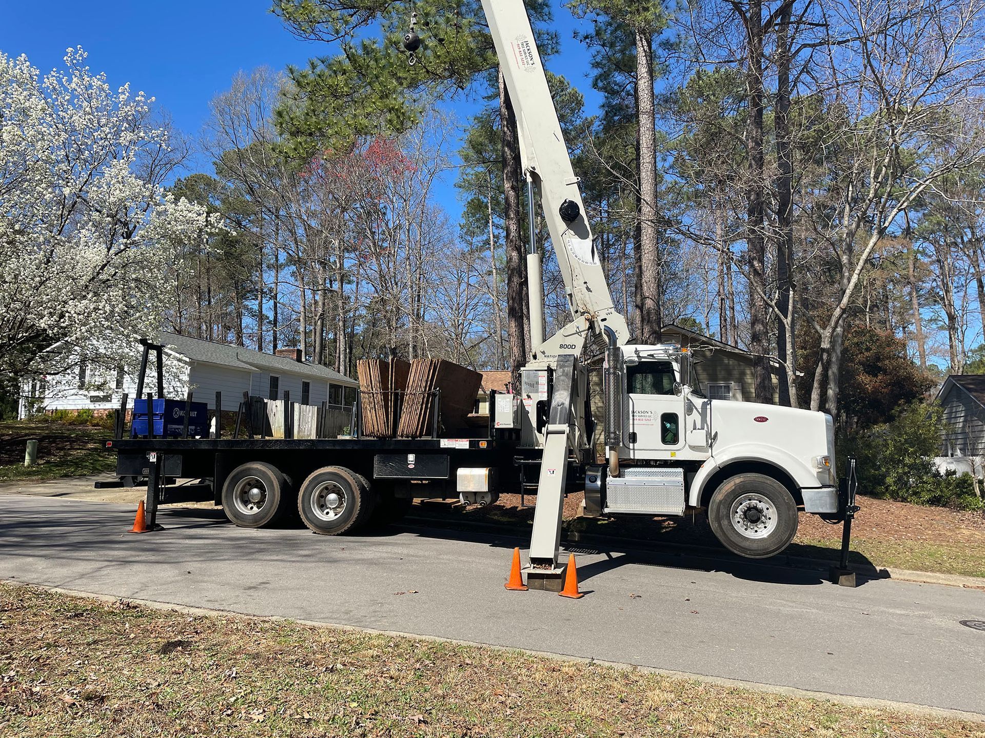 White utility truck with raised boom parked on a road beside trees and a house