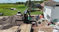 Crane operating at construction site. Workers near a building with equipment and materials. Green field in the background.