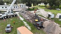 Construction site with crane, excavator, and other machinery working on a long trench in a grassy area.