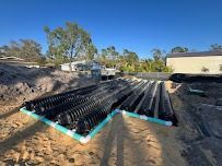 Black corrugated pipes and white PVC piping in an excavated area for a drainage system.