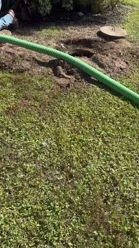 Green hose on a grassy lawn; hole in the ground, possibly a septic tank access point.