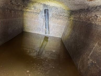 Interior of a concrete tank with a vertical pipe extending into murky water.
