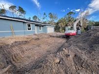 A blue house with a garage has an excavator working on the dirt in front of it on a sunny day.