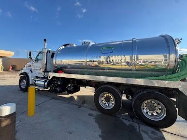 White septic tank truck with a large, shiny silver tank parked outdoors on a sunny day.
