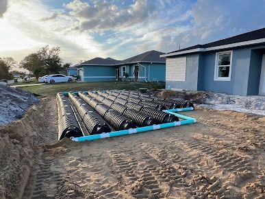 Installation of a septic system on a construction site next to a blue house, featuring black and turquoise drainage components.