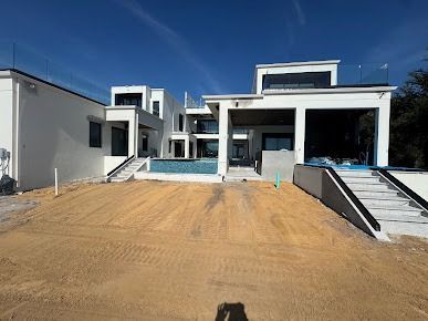 Modern white house with flat roof, pool, and unfinished yard under a clear blue sky.